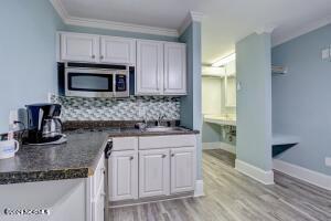 kitchen featuring stainless steel microwave, a sink, backsplash, and white cabinetry