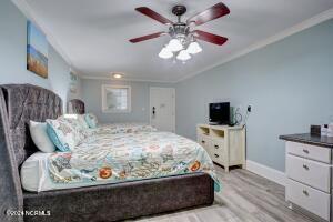 bedroom featuring light wood-style floors, crown molding, vaulted ceiling, and baseboards