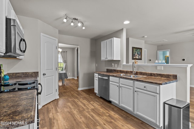 kitchen with appliances with stainless steel finishes, track lighting, sink, white cabinetry, and hardwood / wood-style flooring