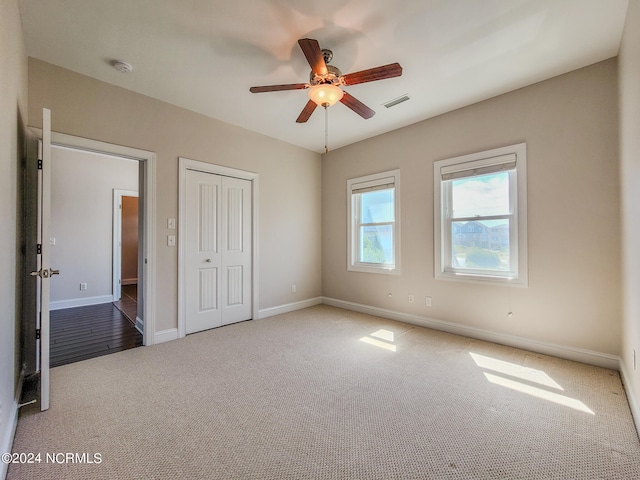 unfurnished bedroom featuring a closet, light colored carpet, and ceiling fan