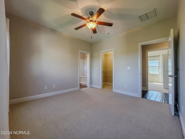 unfurnished bedroom with ceiling fan, light carpet, a closet, and a walk in closet