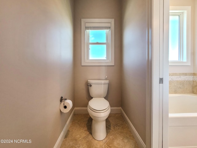 bathroom featuring toilet, a bathing tub, and plenty of natural light