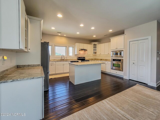 kitchen featuring stainless steel appliances, dark hardwood / wood-style flooring, white cabinets, light stone countertops, and a kitchen island