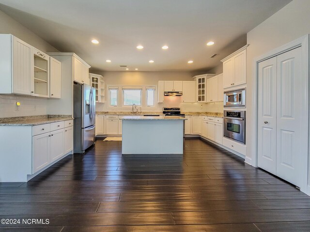 kitchen with appliances with stainless steel finishes, sink, a kitchen island, white cabinetry, and dark wood-type flooring