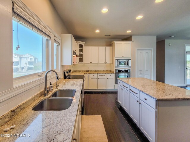 kitchen featuring stainless steel appliances, sink, white cabinetry, a center island, and dark wood-type flooring