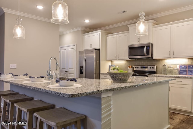 kitchen featuring pendant lighting, stainless steel appliances, an island with sink, and white cabinetry