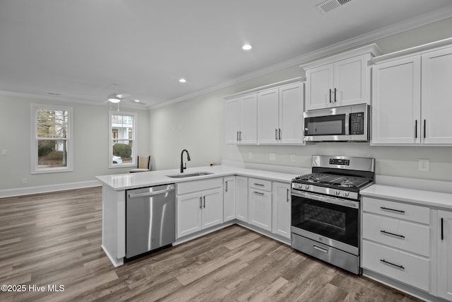 kitchen with ornamental molding, a sink, wood finished floors, white cabinetry, and stainless steel appliances