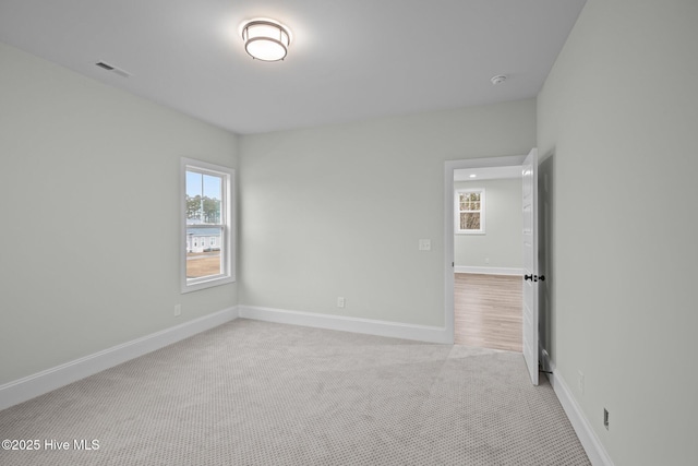 spare room featuring light colored carpet, visible vents, and baseboards