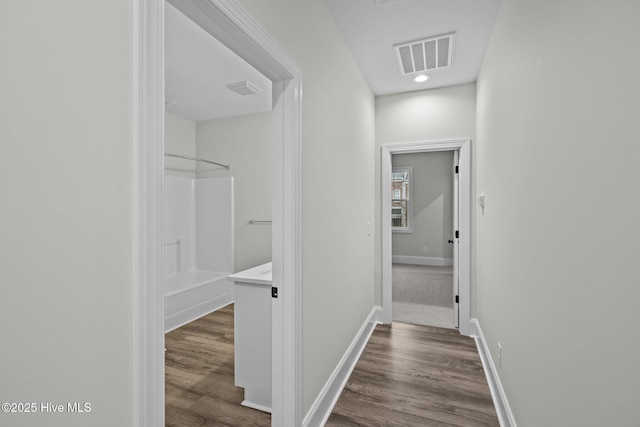 hall featuring visible vents, baseboards, and wood finished floors