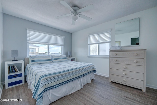 bedroom with ceiling fan, multiple windows, a textured ceiling, and hardwood / wood-style floors