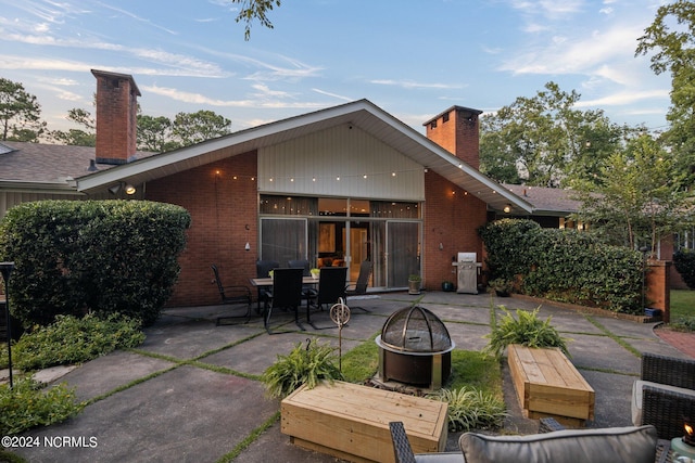 rear view of property with a patio area, an outdoor fire pit, a chimney, and brick siding