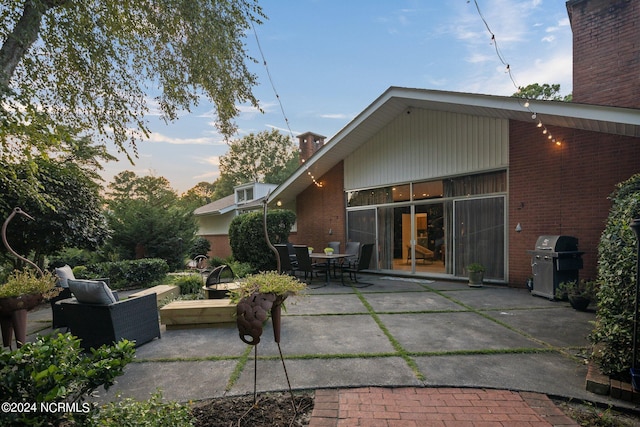 back of house featuring brick siding, a chimney, and a patio