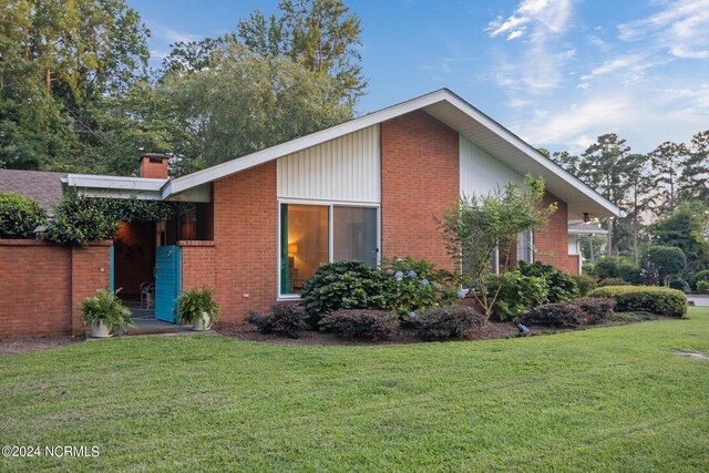 view of property exterior featuring brick siding, a lawn, and a chimney