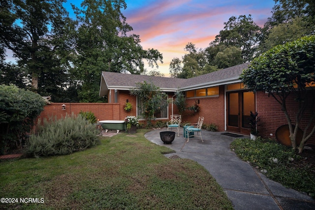 back of property at dusk featuring a yard, a patio area, fence, and brick siding