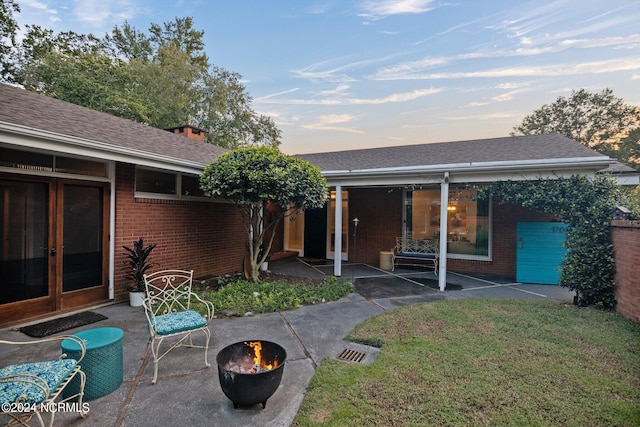 back of house at dusk with brick siding, a fire pit, and french doors