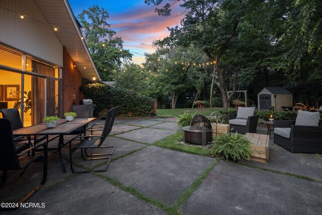 view of patio with a fire pit, a shed, outdoor dining space, and an outbuilding