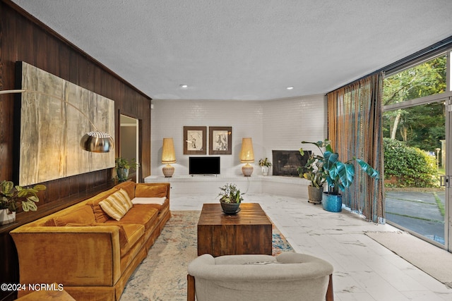 living area featuring marble finish floor, wood walls, a fireplace, and a textured ceiling