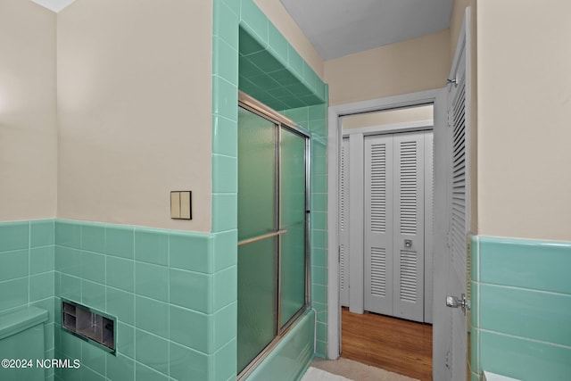 full bath with a closet, wainscoting, toilet, combined bath / shower with glass door, and tile walls