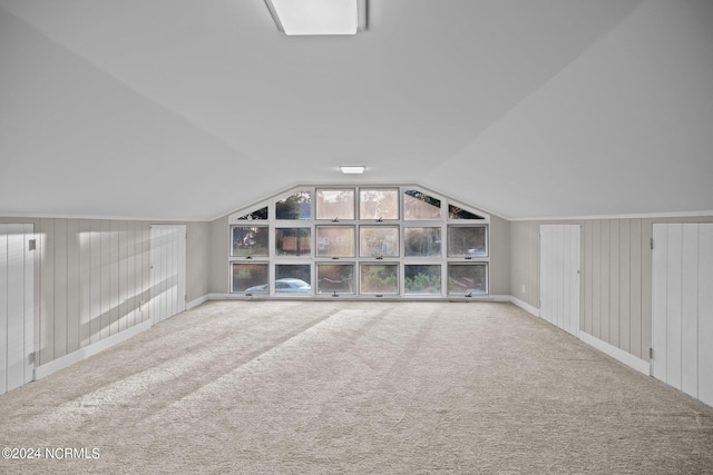 bonus room with carpet floors, lofted ceiling, and wood walls