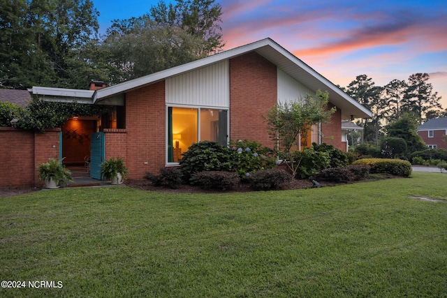 property exterior at dusk featuring brick siding and a yard