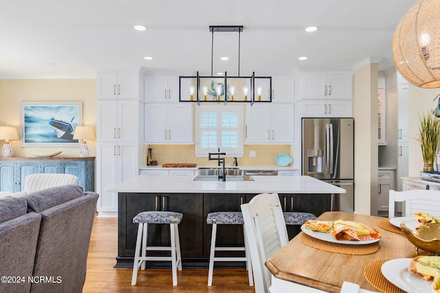 kitchen with hanging light fixtures, an island with sink, white cabinets, and stainless steel fridge