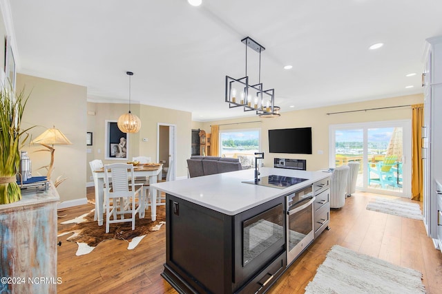 kitchen with hanging light fixtures, black appliances, light hardwood / wood-style floors, and a center island with sink