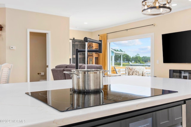 kitchen with hanging light fixtures, black electric cooktop, ornamental molding, a notable chandelier, and light stone countertops