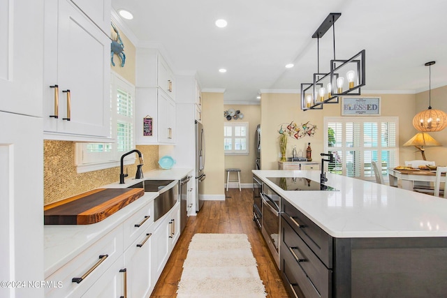 kitchen featuring sink, hanging light fixtures, an island with sink, white cabinets, and black electric cooktop