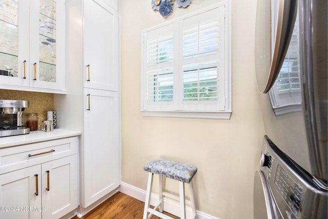 interior space featuring stacked washer and dryer, white cabinetry, backsplash, and light hardwood / wood-style floors