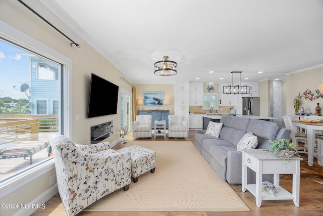 living room featuring crown molding, a wealth of natural light, an inviting chandelier, and light hardwood / wood-style floors