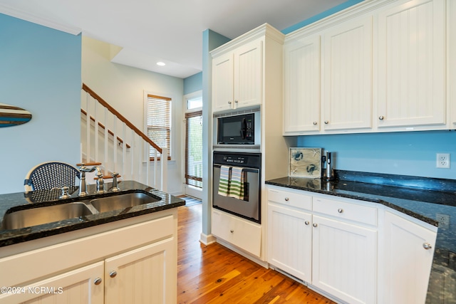 kitchen with black microwave, sink, oven, light wood-type flooring, and dark stone countertops