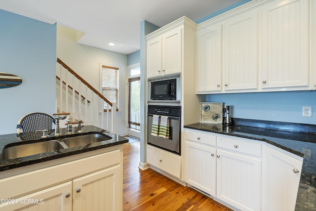 kitchen featuring black microwave, sink, dark stone countertops, white cabinets, and stainless steel oven