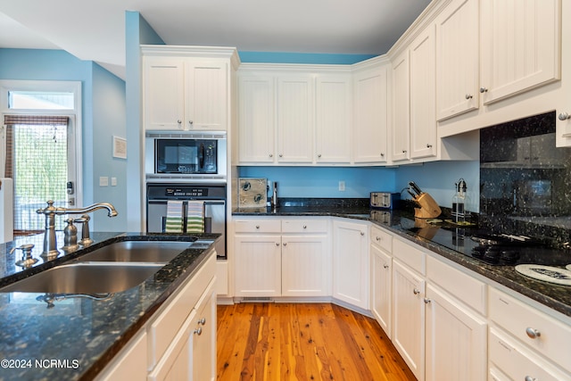 kitchen featuring light hardwood / wood-style flooring, black microwave, dark stone counters, sink, and oven