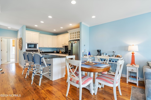 kitchen with light hardwood / wood-style flooring, black microwave, a breakfast bar, oven, and stainless steel refrigerator with ice dispenser