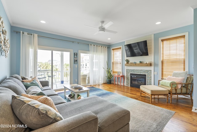 living room with crown molding, ceiling fan, wood-type flooring, and a tiled fireplace