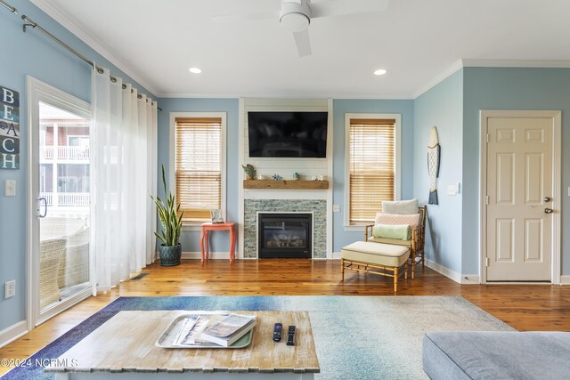 living room with crown molding, a stone fireplace, hardwood / wood-style floors, and ceiling fan