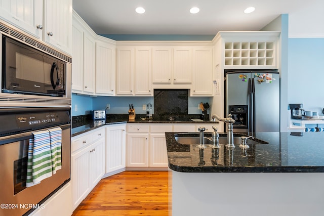 kitchen featuring appliances with stainless steel finishes, dark stone counters, sink, light hardwood / wood-style floors, and white cabinetry