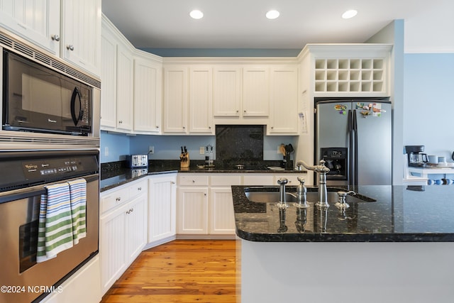 kitchen featuring sink, light hardwood / wood-style flooring, appliances with stainless steel finishes, white cabinetry, and dark stone counters