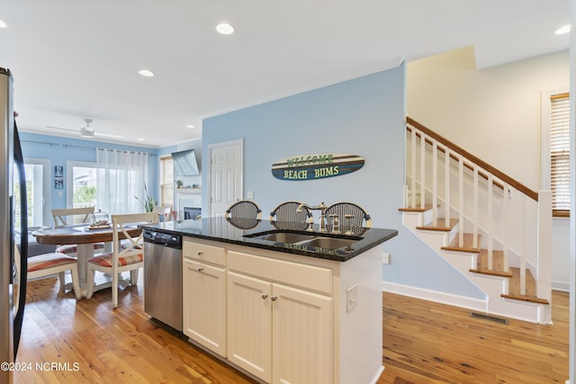 kitchen with an island with sink, sink, dark stone counters, hardwood / wood-style flooring, and stainless steel dishwasher