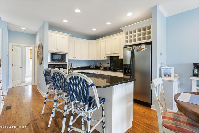 kitchen with a kitchen bar, black appliances, light wood-type flooring, dark stone countertops, and a center island