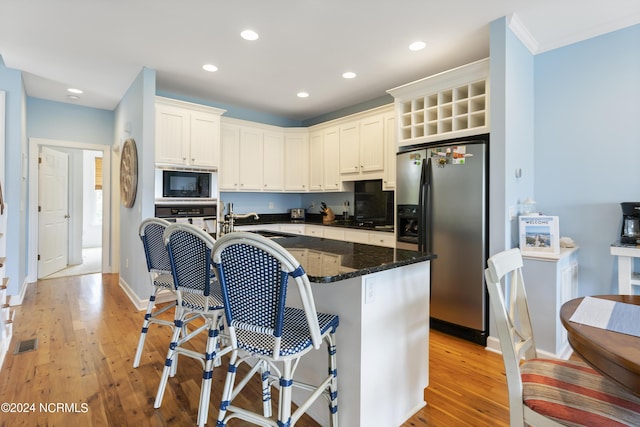 kitchen with sink, white cabinetry, light wood-type flooring, dark stone counters, and stainless steel appliances