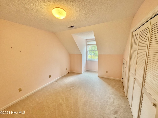 additional living space with lofted ceiling, light colored carpet, visible vents, a textured ceiling, and baseboards