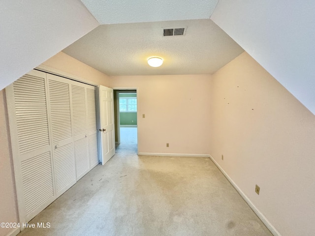 unfurnished bedroom featuring visible vents, baseboards, light colored carpet, a textured ceiling, and a closet