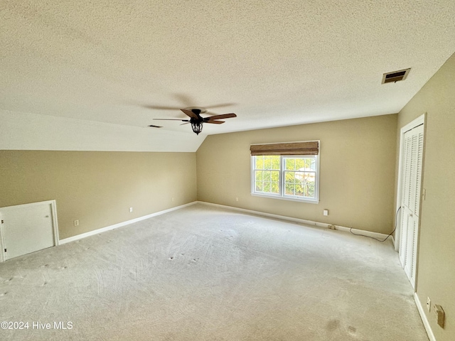 additional living space featuring lofted ceiling, light colored carpet, visible vents, a textured ceiling, and baseboards