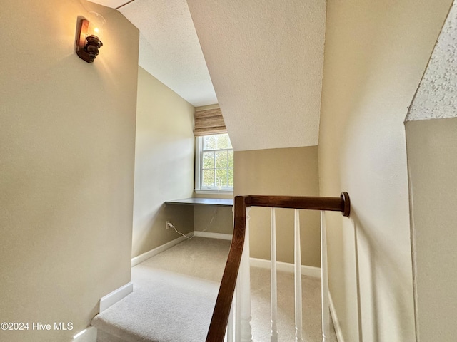 staircase with carpet floors, built in desk, lofted ceiling, a textured ceiling, and baseboards