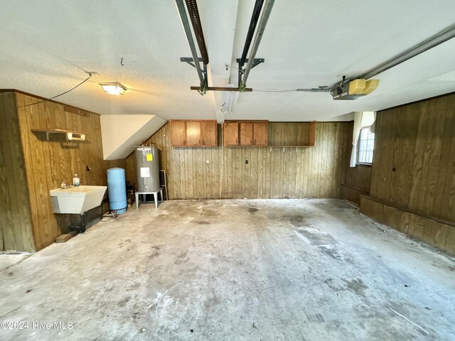 garage with a garage door opener, a sink, electric water heater, and wooden walls