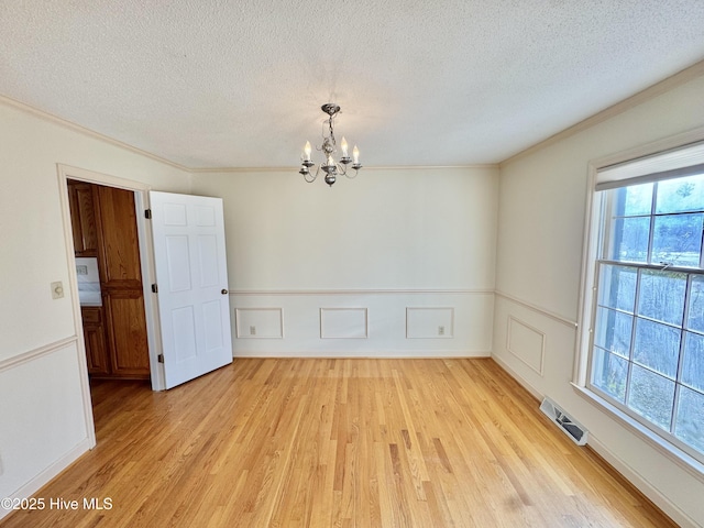 empty room featuring visible vents, wainscoting, crown molding, light wood-type flooring, and a notable chandelier