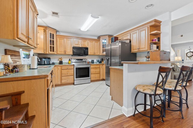 kitchen featuring light brown cabinets, light hardwood / wood-style floors, appliances with stainless steel finishes, kitchen peninsula, and a kitchen breakfast bar