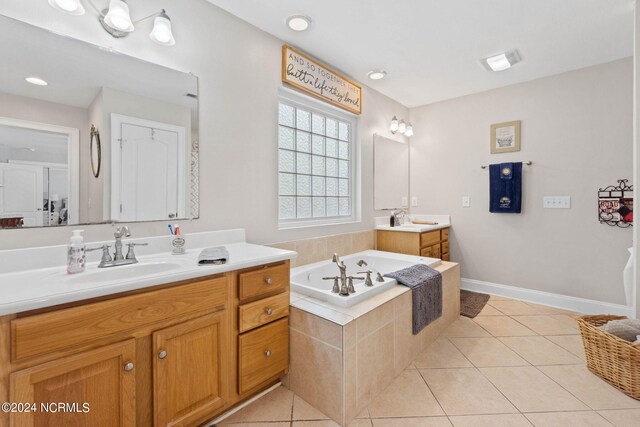 bathroom featuring a relaxing tiled tub, dual bowl vanity, and tile patterned floors