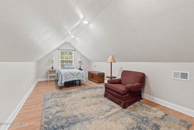 bedroom with a textured ceiling, light hardwood / wood-style flooring, and lofted ceiling